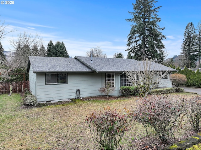 view of front of property with a front yard, roof with shingles, and fence