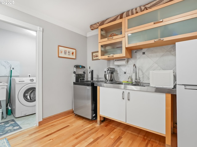 kitchen with washer / clothes dryer, freestanding refrigerator, a sink, stainless steel countertops, and tasteful backsplash