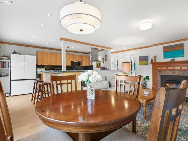 dining area featuring a premium fireplace, recessed lighting, light wood-type flooring, and ornamental molding