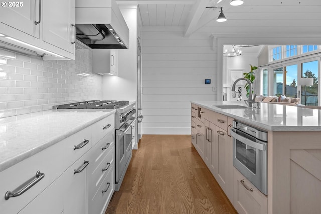 kitchen featuring premium range hood, beamed ceiling, white cabinetry, sink, and stainless steel appliances