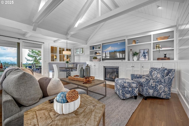 living room featuring lofted ceiling with beams, built in shelves, hardwood / wood-style floors, and a brick fireplace