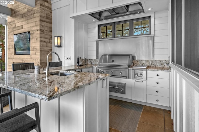 kitchen with sink, custom exhaust hood, a breakfast bar area, white cabinetry, and light stone countertops