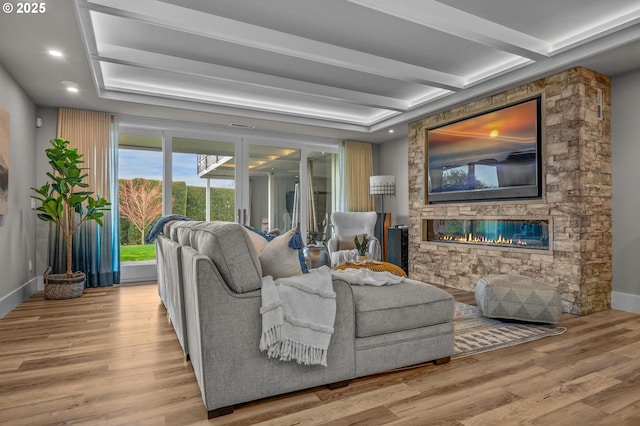 living room with beamed ceiling, a stone fireplace, and light hardwood / wood-style floors