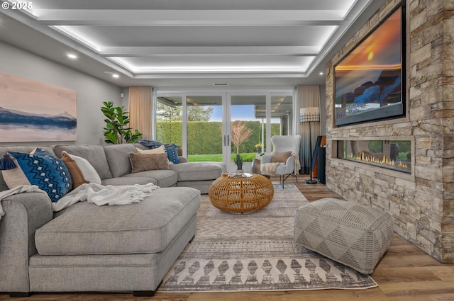 living room with a raised ceiling, a stone fireplace, and light wood-type flooring