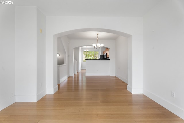 736 NW 118th Ave Unit 102, Portland, OR 97229 - unfurnished dining area featuring a chandelier, arched walkways, light wood-style flooring, and baseboards