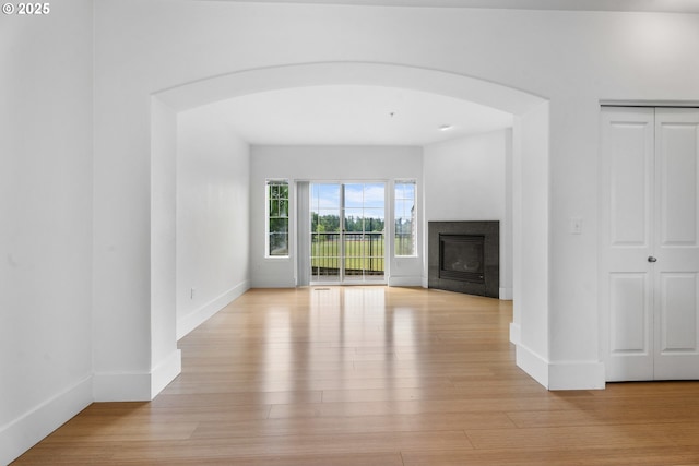 736 NW 118th Ave Unit 102, Portland, OR 97229 - unfurnished living room featuring arched walkways, light wood-style floors, a glass covered fireplace, and baseboards