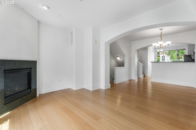 736 NW 118th Ave Unit 102, Portland, OR 97229 - unfurnished living room with a tile fireplace, wood finished floors, a chandelier, arched walkways, and baseboards