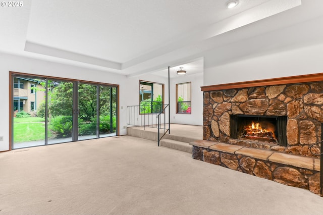 unfurnished living room with carpet flooring, a tray ceiling, and a fireplace