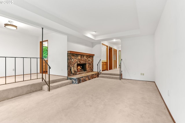 unfurnished living room with carpet flooring, a tray ceiling, stairway, a fireplace, and baseboards