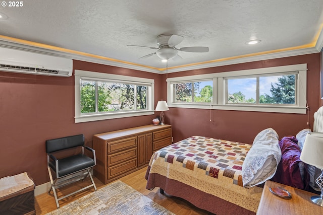 bedroom with an AC wall unit, multiple windows, light wood finished floors, ornamental molding, and a textured ceiling