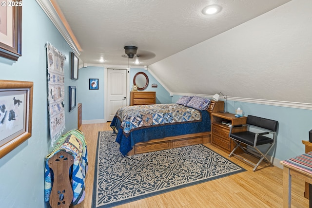 bedroom with wood finished floors, a textured ceiling, lofted ceiling, ceiling fan, and ornamental molding