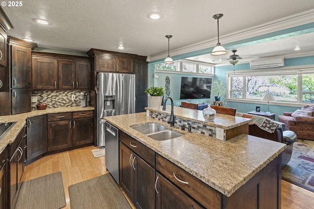 kitchen with a sink, a wall mounted air conditioner, open floor plan, stainless steel appliances, and light wood finished floors