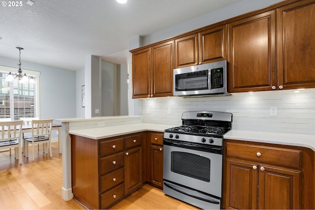 kitchen with light wood-style flooring, appliances with stainless steel finishes, a peninsula, and light countertops