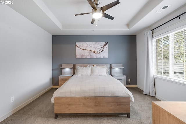 carpeted bedroom with a ceiling fan, a raised ceiling, baseboards, and visible vents