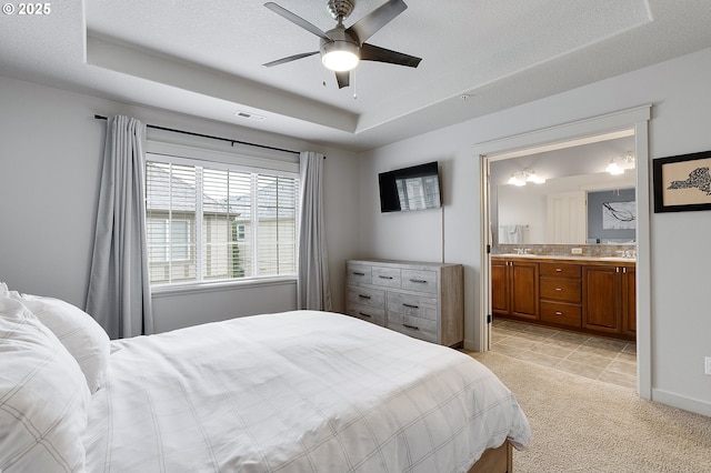 bedroom featuring visible vents, connected bathroom, light colored carpet, a textured ceiling, and a raised ceiling