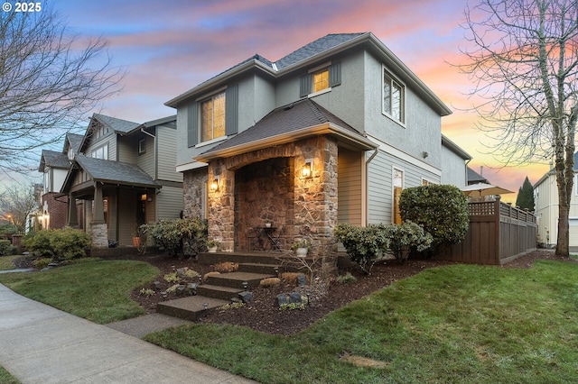 view of front of house featuring stone siding, roof with shingles, a front lawn, and fence