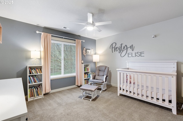 carpeted bedroom featuring visible vents, baseboards, a nursery area, and a ceiling fan