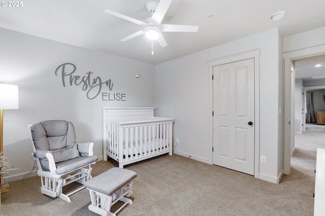 bedroom featuring a nursery area, baseboards, carpet, and ceiling fan