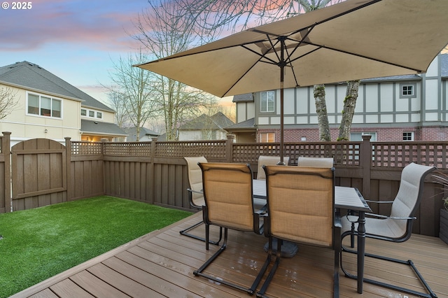 wooden terrace featuring outdoor dining area, a lawn, and a fenced backyard