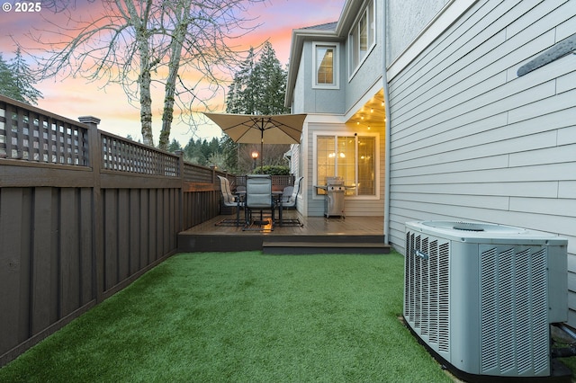 yard at dusk with central air condition unit, a wooden deck, outdoor dining space, and fence