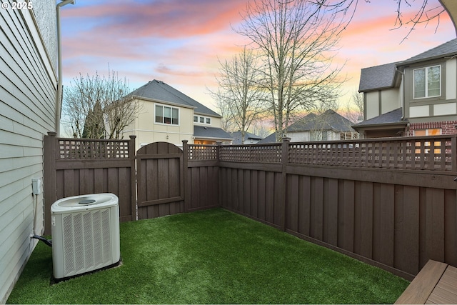 yard at dusk featuring central AC, a fenced backyard, and a gate