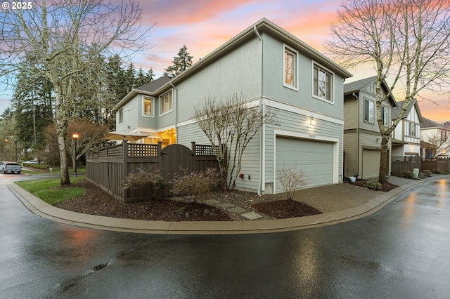 view of side of home with stucco siding, driveway, a garage, and fence