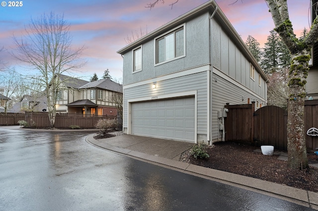 property exterior at dusk featuring concrete driveway, an attached garage, fence, and stucco siding