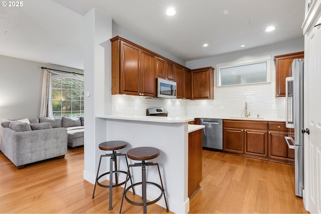 kitchen featuring a kitchen bar, light wood-style flooring, a sink, a peninsula, and appliances with stainless steel finishes