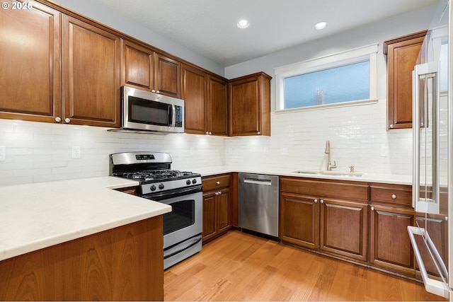 kitchen with light wood-style flooring, stainless steel appliances, light countertops, and a sink