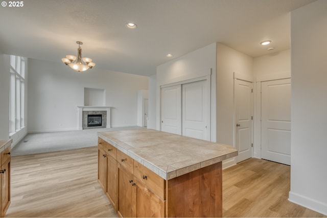 kitchen featuring light wood-type flooring, a notable chandelier, a glass covered fireplace, recessed lighting, and tile counters