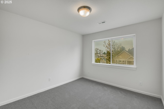 spare room featuring visible vents, baseboards, and dark carpet