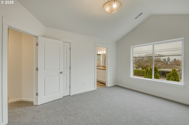 unfurnished bedroom featuring visible vents, baseboards, vaulted ceiling, light carpet, and ensuite bathroom