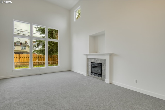 unfurnished living room with a tiled fireplace, a towering ceiling, baseboards, and carpet floors