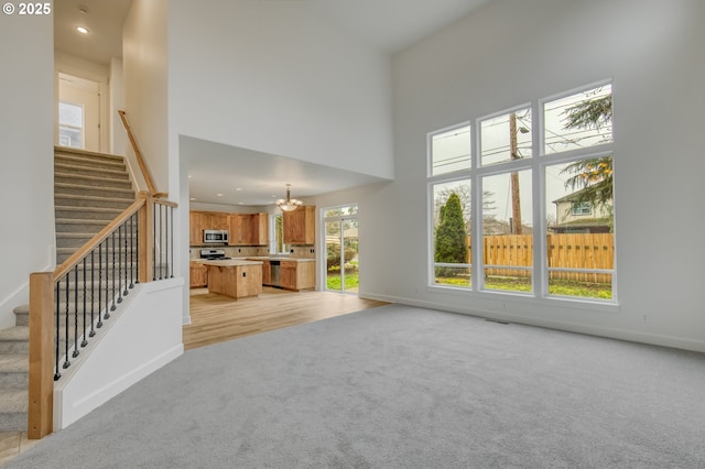 unfurnished living room featuring stairway, baseboards, an inviting chandelier, a towering ceiling, and light colored carpet