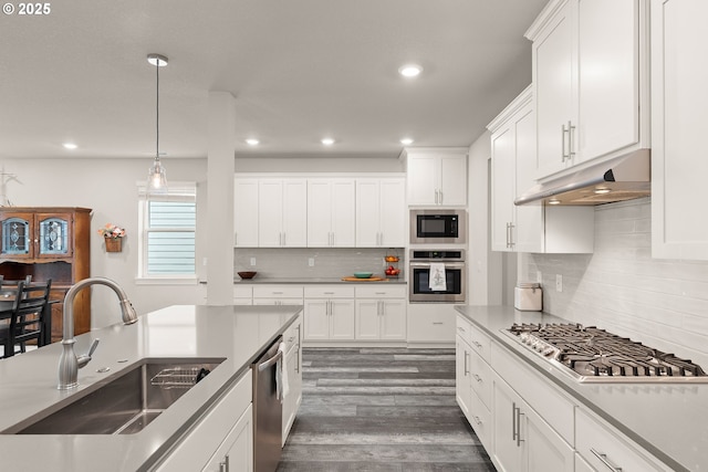 kitchen with dark wood-style flooring, stainless steel appliances, white cabinetry, a sink, and under cabinet range hood