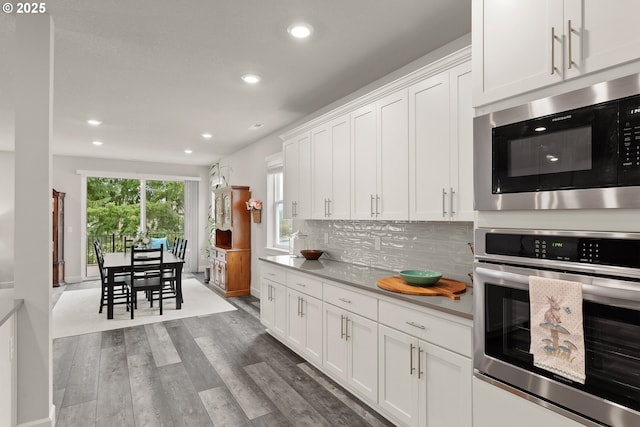 kitchen with built in microwave, wood finished floors, stainless steel oven, white cabinets, and decorative backsplash