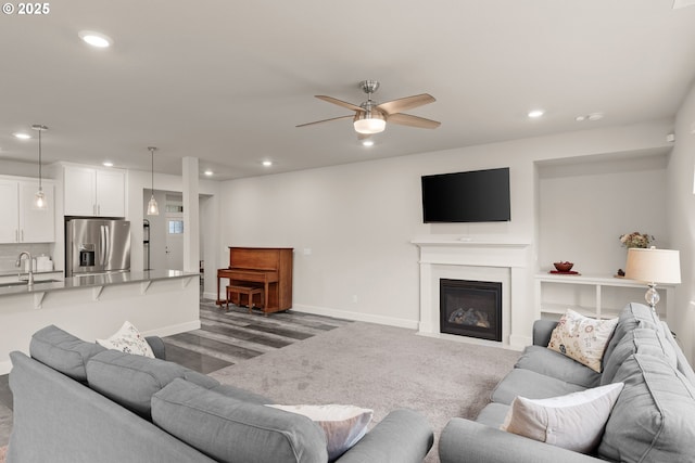 living area with baseboards, a glass covered fireplace, a ceiling fan, and recessed lighting