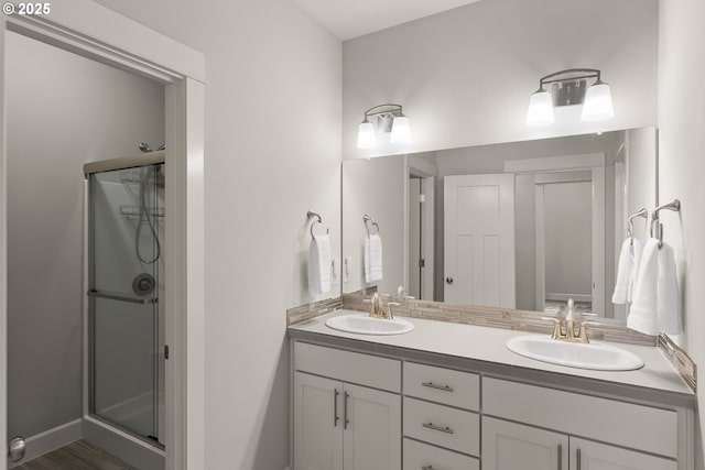 bathroom featuring double vanity, a stall shower, a sink, and baseboards