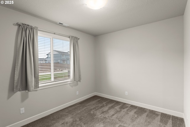 empty room with visible vents, dark carpet, a textured ceiling, and baseboards