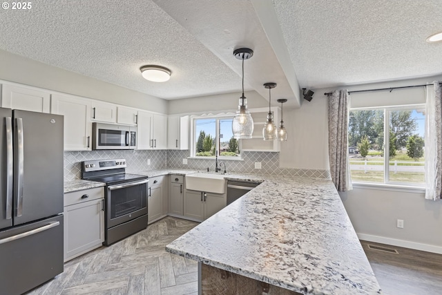 33549 Wikstrom Rd, Scappoose, OR 97056 - kitchen with appliances with stainless steel finishes, plenty of natural light, a peninsula, a textured ceiling, and backsplash