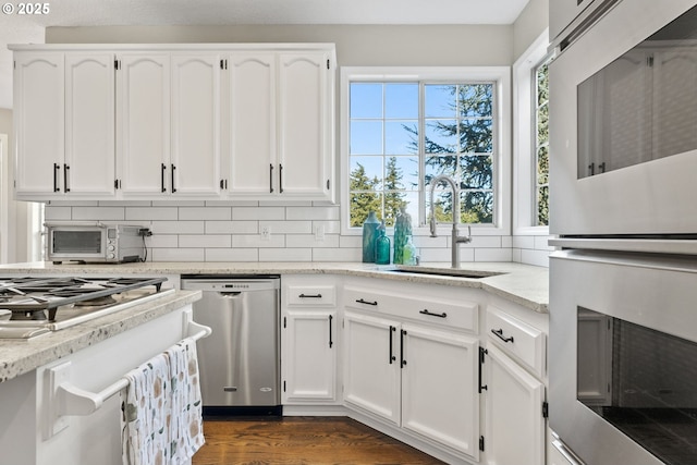 kitchen featuring sink, appliances with stainless steel finishes, white cabinetry, tasteful backsplash, and light stone countertops