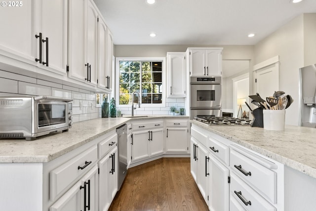 kitchen with sink, appliances with stainless steel finishes, white cabinetry, dark hardwood / wood-style floors, and decorative backsplash