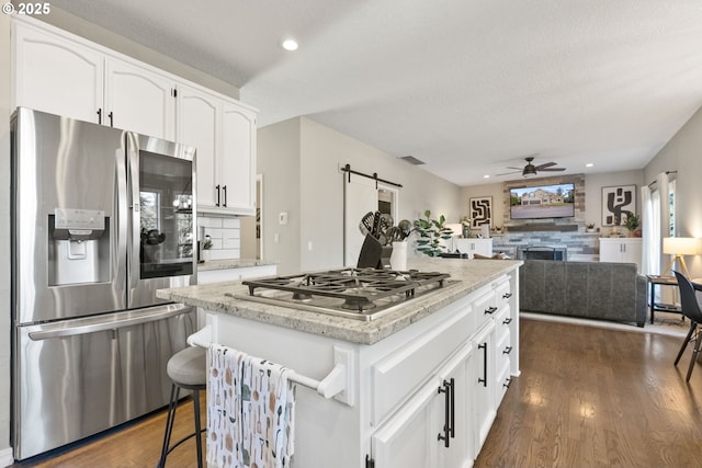 kitchen with a kitchen breakfast bar, stainless steel appliances, white cabinets, a kitchen island, and a barn door