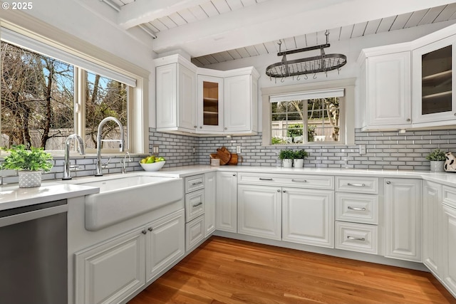kitchen featuring stainless steel dishwasher, decorative backsplash, beamed ceiling, a sink, and white cabinets