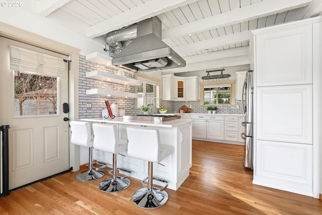 kitchen featuring a kitchen bar, island range hood, kitchen peninsula, decorative backsplash, and white cabinets