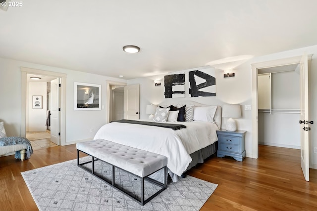bedroom featuring wood finished floors, a walk in closet, baseboards, and a closet