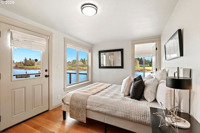 bedroom with wood finished floors, multiple windows, and a water view