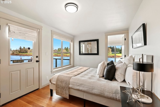 bedroom featuring a water view, access to exterior, and light wood-type flooring