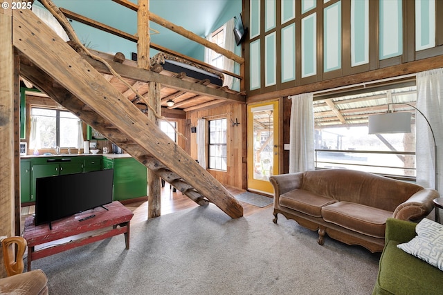 living room featuring high vaulted ceiling, wood walls, and carpet floors