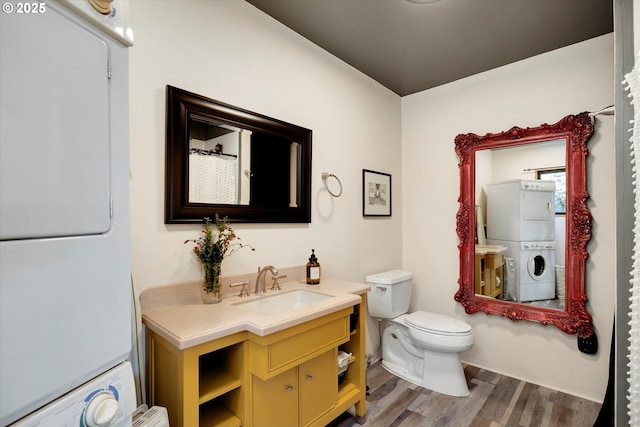 bathroom with toilet, stacked washing maching and dryer, wood finished floors, and vanity